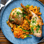 Overhead traditional Valencian paella with chicken thighs and rabbit leg served on a blue plate.