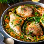 Paella Valenciana with rabbit and chicken presented in a traditional cooking pan featuring a title overlay.