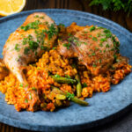 Traditional Valencian paella with chicken thighs and rabbit legs served on a blue plate.