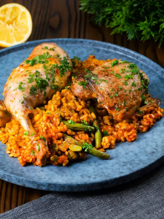 Traditional Valencian paella with chicken thighs and rabbit legs served on a blue plate.