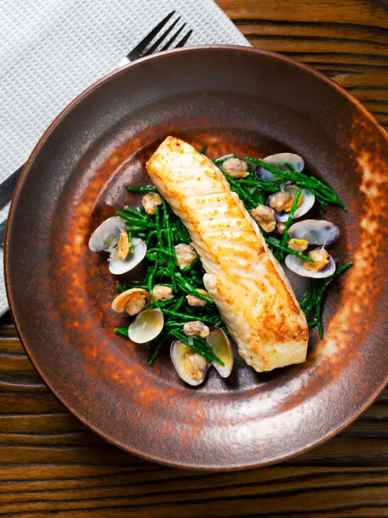 Overhead pan fried halibut fillet with clams and samphire in white wine sauce.