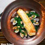 Overhead pan fried halibut fillet with clams and samphire in white wine sauce featuring a title overlay.