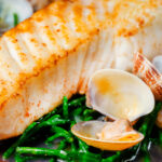 Close-up clams and samphire served with golden fried halibut fillet.
