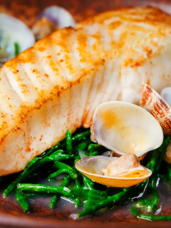 Close-up clams and samphire served with golden fried halibut fillet.