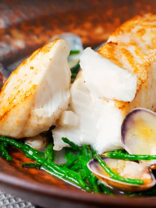 Pan fried halibut fillet with clams and samphire opened to show the white flesh.