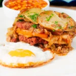 Layered corned beef and potato bake or panacalty with a fried egg and baked beans.