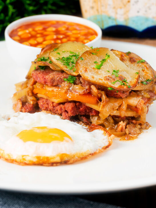 Layered corned beef and potato bake or panacalty with a fried egg and baked beans.