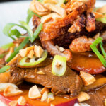 Close-up plum and duck stir fry with crispy skin, toasted peanuts and spring onions.