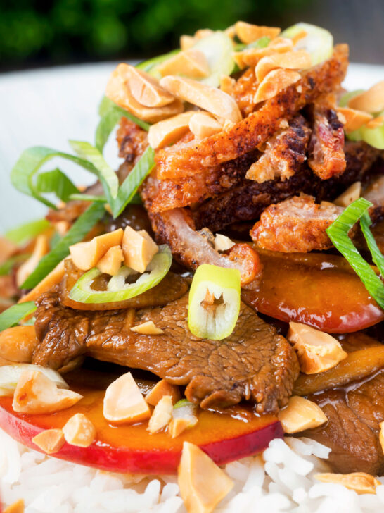 Close-up plum and duck stir fry with crispy skin, toasted peanuts and spring onions.