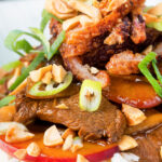 Close-up plum and duck stir fry with crispy skin, toasted peanuts and spring onions featuring a title overlay.