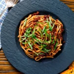 Overhead vegan red lentil bolognese served with fresh basil and garlic bread.