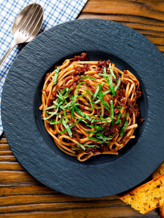 Overhead vegan red lentil bolognese served with fresh basil and garlic bread.