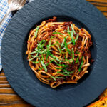 Overhead vegan red lentil bolognese served with fresh basil and garlic bread featuring a title overlay.