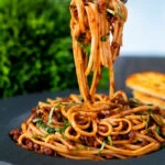 Vegan red lentil bolognese with linguini pasta being picked up with a fork.