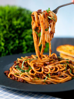 Vegan red lentil bolognese with linguini pasta being picked up with a fork.