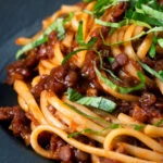 Close-up vegan red lentil ragu with linguini pasta and fresh basil.