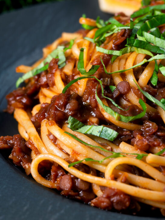 Close-up vegan red lentil ragu with linguini pasta and fresh basil.