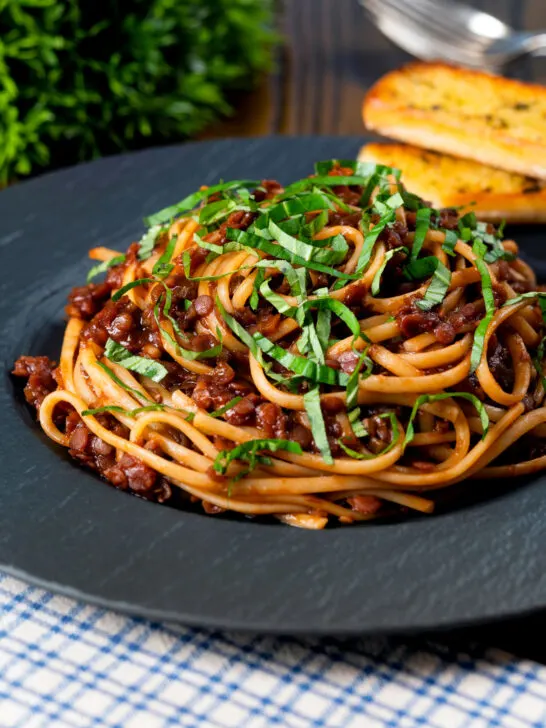 Vegan red lentil bolognese served with fresh basil and garlic bread.