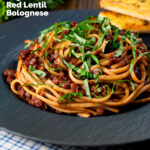 Vegan red lentil bolognese served with fresh basil and garlic bread featuring a title overlay.