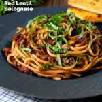 Vegan red lentil bolognese served with fresh basil and garlic bread featuring a title overlay.