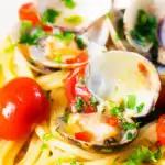 Close-up spaghetti alle vongole or clam pasta with tomatoes, parsley and garlic featuring a title overlay.