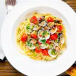 Overhead spaghetti alle vongole or clam pasta with tomatoes, parsley and garlic featuring a title overlay.