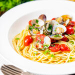 Spaghetti alle vongole or clam pasta with tomatoes, parsley and garlic featuring a title overlay.