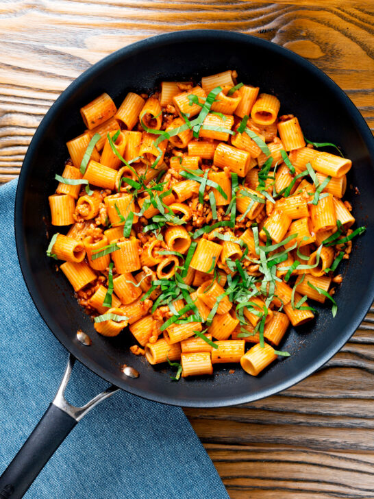 Overhead spicy ground chicken rigatoni with fresh basil in a pan.