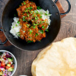 Overhead beef bhuna or bhuna gosht curry with poppadoms, raita and kachumber salad.