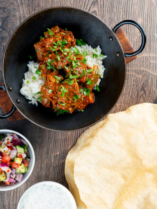 Overhead beef bhuna or bhuna gosht curry with poppadoms, raita and kachumber salad.