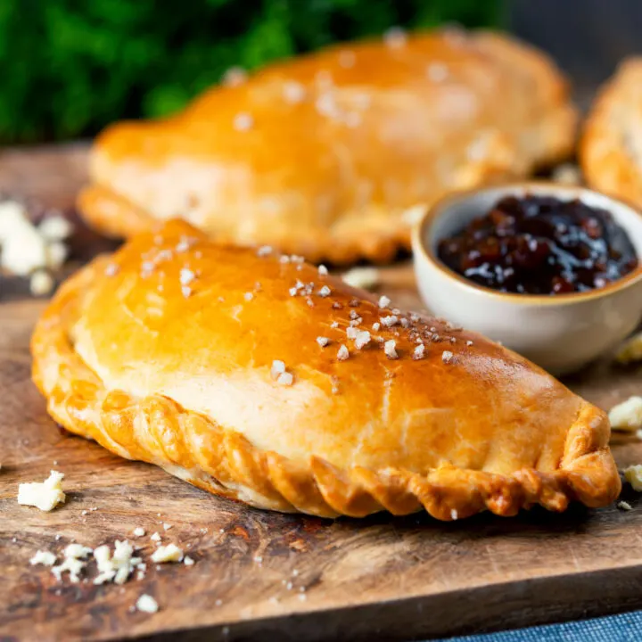 Homemade cheese and onion pasty with added Branston Pickle served on a board.