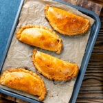 Overhead homemade cheese and onion pasties in shortcrust pastry on a baking sheet.