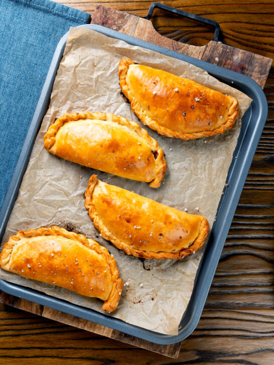 Overhead homemade cheese and onion pasties in shortcrust pastry on a baking sheet.