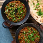 Overhead Indian chicken keema curry with green beans served with naan bread.