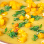 Close-up curried cauliflower veloute soup garnished with turmeric potatoes and coriander.
