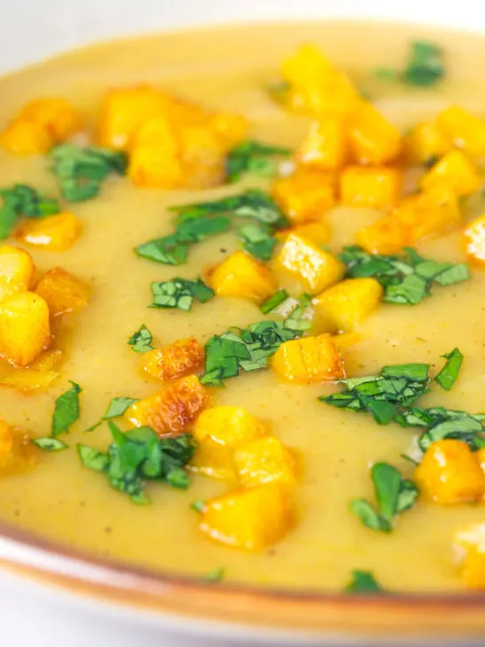 Close-up curried cauliflower veloute soup garnished with turmeric potatoes and coriander.