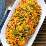 Overhead giant couscous salad with rose harissa paste and oranges.