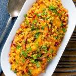 Overhead giant couscous salad with rose harissa paste and oranges.