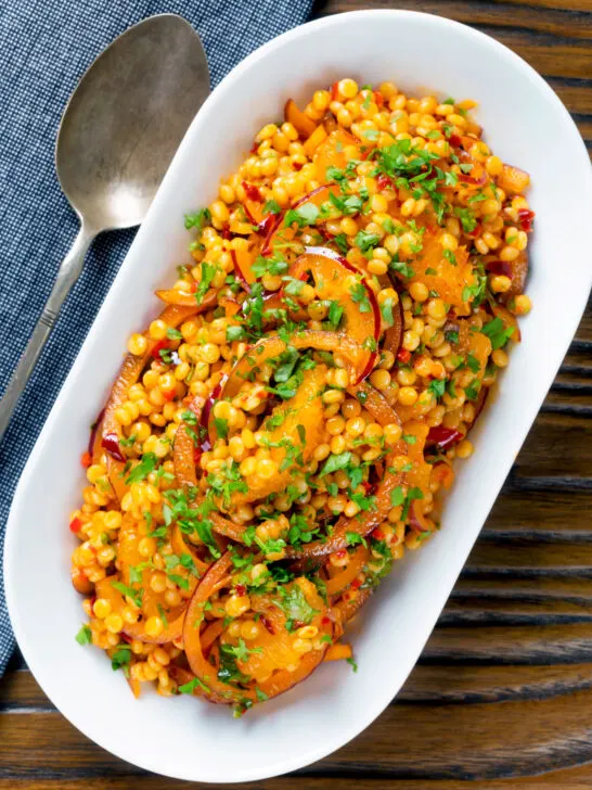 Overhead giant couscous salad with rose harissa paste and oranges.