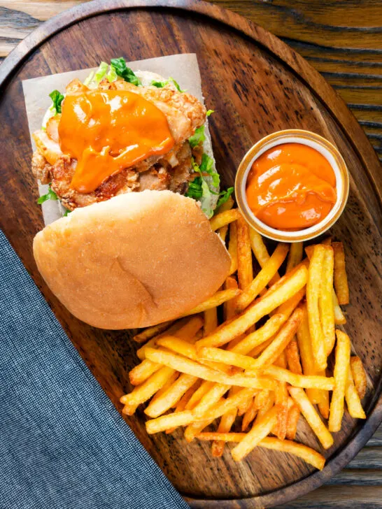 Overhead Korean fried chicken burger with gochujang mayo and kimchi served with fries.