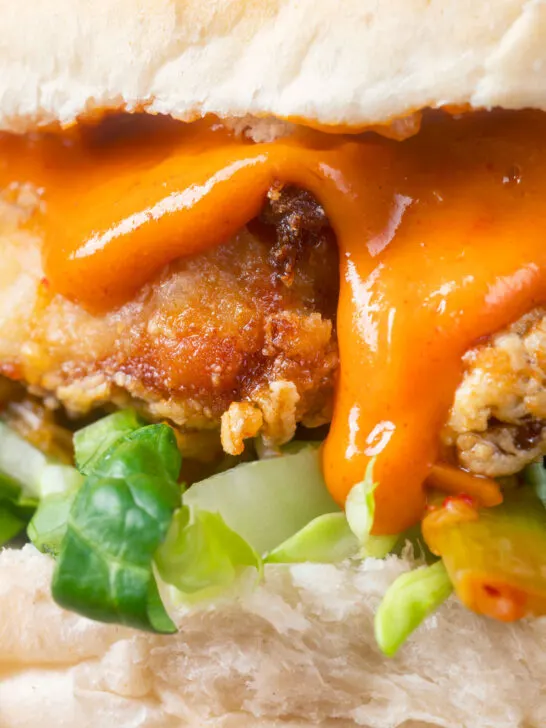 Close-up Korean-influenced crispy fried chicken burger with gochujang mayo.