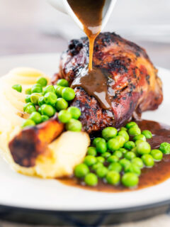 Gravy being poured over minted lamb shanks served with peas and mashed potato.