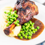 Oven cooked minted lamb shanks served with peas, mashed potato and red wine gravy featuring a title overlay.