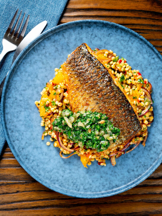 Overhead pan fried grey mullet fillet served with preserved lemons and parsley and giant couscous.