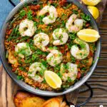 Overhead prawn and chorizo paella served in a paella pan with lemon and parsley featuring a title overlay.