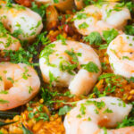 Close-up prawn and chorizo paella served in a paella pan with lemon and parsley.
