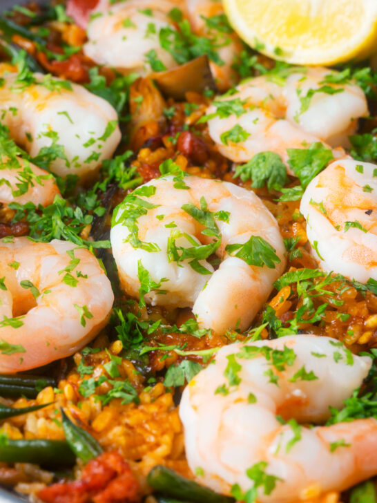 Close-up prawn and chorizo paella served in a paella pan with lemon and parsley.