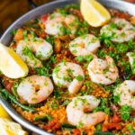 Prawn and chorizo paella served in a paella pan with lemon and parsley.
