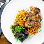 Overhead oven roasted cauliflower steak served with giant couscous salad.