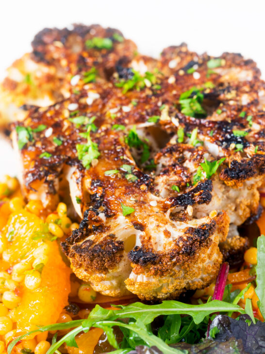 Close-up oven roasted cauliflower steak served with giant couscous salad.